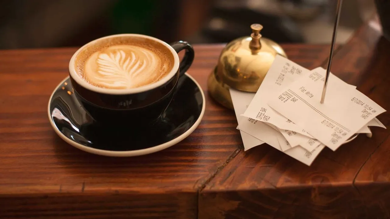 Tasse Kaffee neben einem Stapel aufgespießter Belege auf einem Holztresen